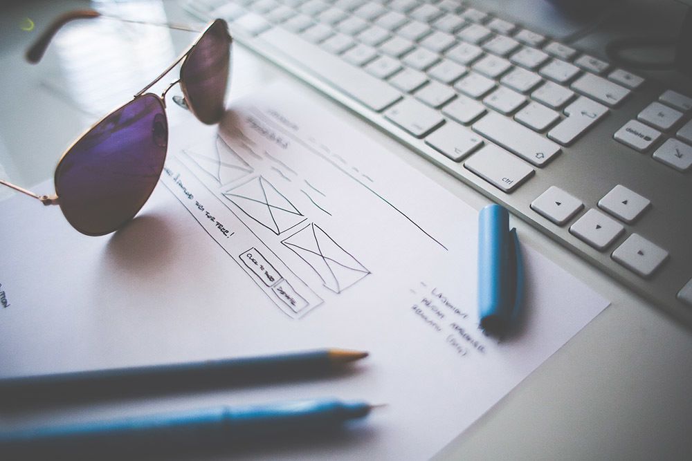 A keyboard, a pair of sunglasses, a UX sketch and some pencils